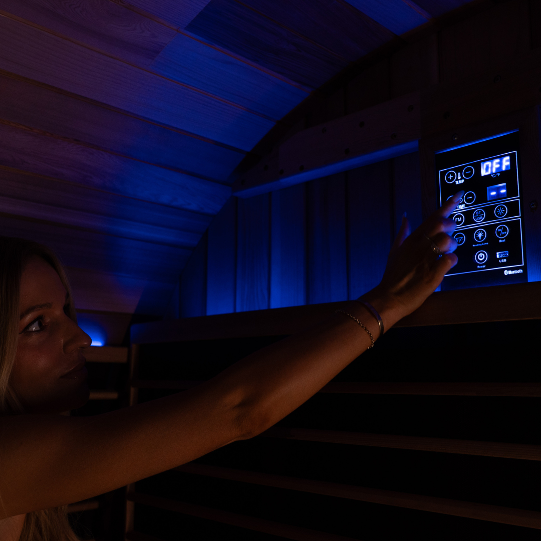 Person adjusting controls on a dark infrared sauna interior with touch control panel