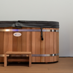 Wooden hot tub with a black cover and metal bands on a wooden floor.