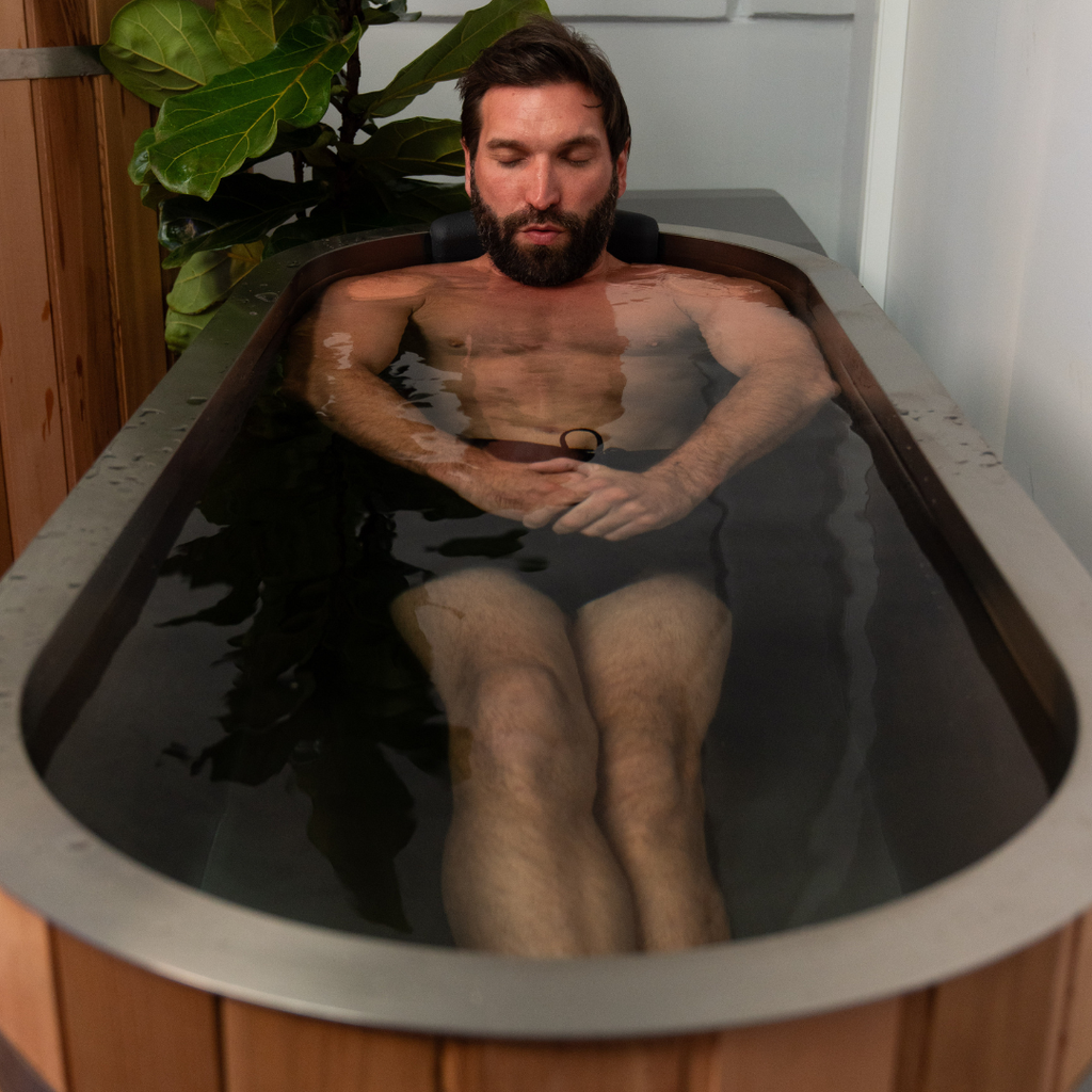 Man sitting in a wooden ice bath with plants around