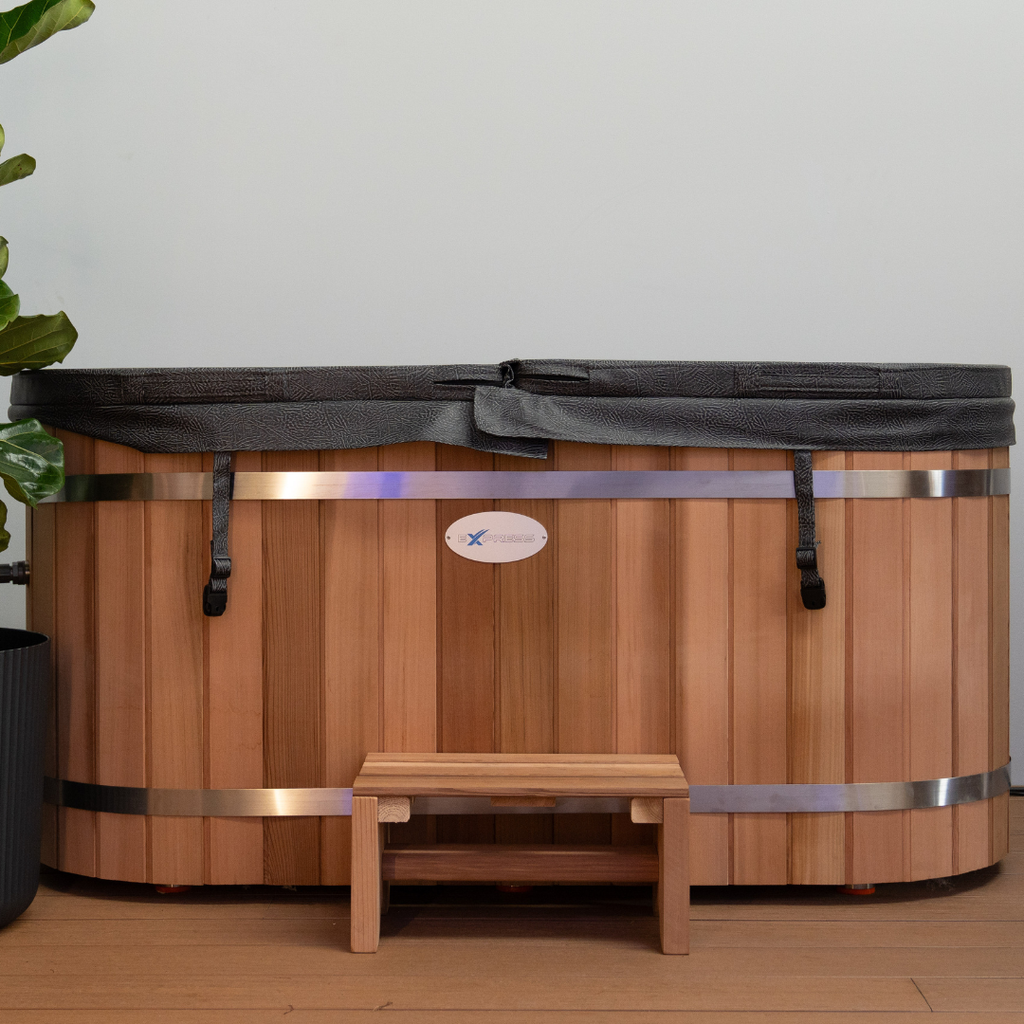 Wooden hot tub with a bench on a wooden floor against a white wall.