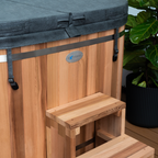 Wooden hot tub with a step and blue cover, featuring a brand logo.
