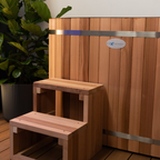Wooden steps leading up to a wooden hot tub with a brand logo on a wooden deck.