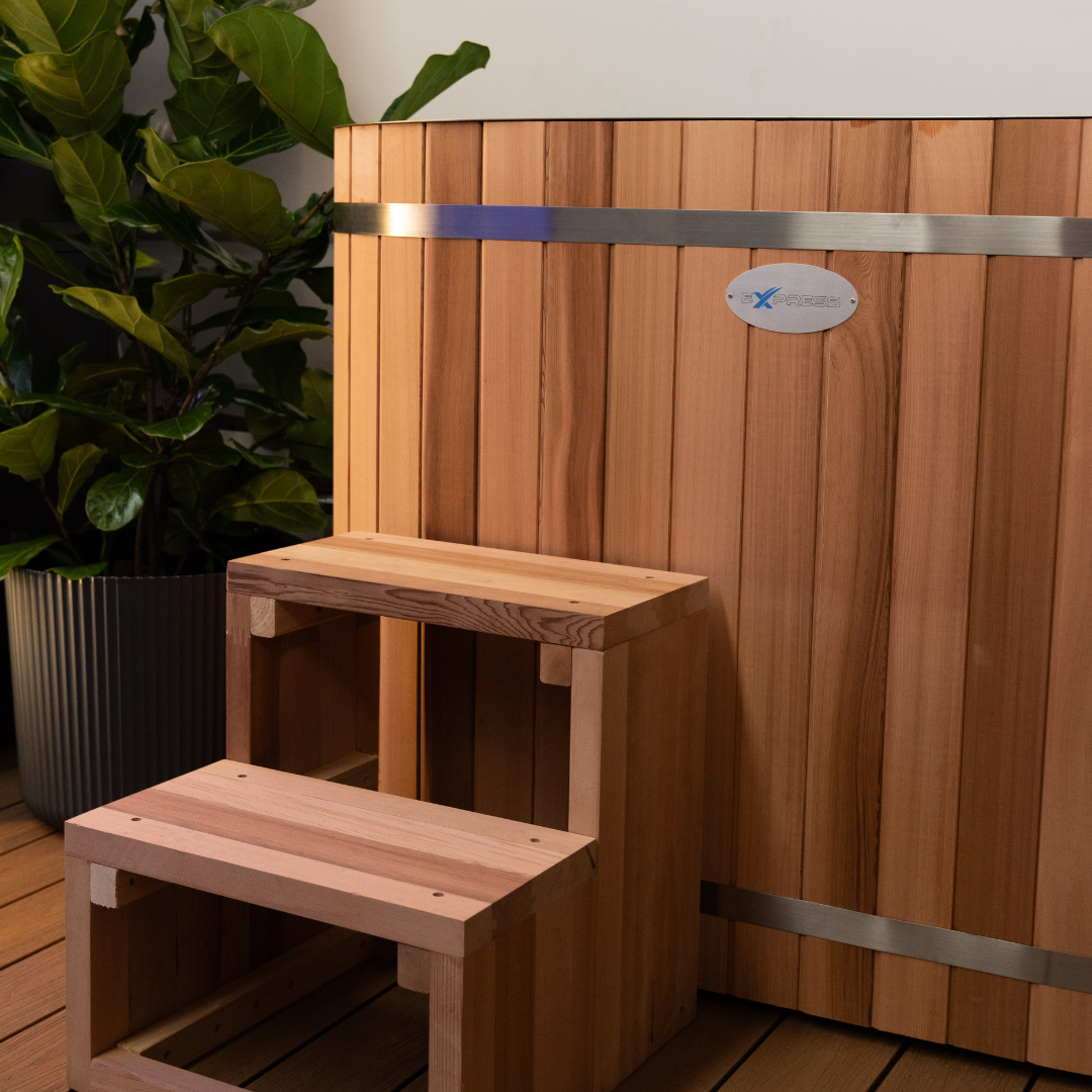 Wooden steps leading up to a wooden hot tub with a brand logo on a wooden deck.