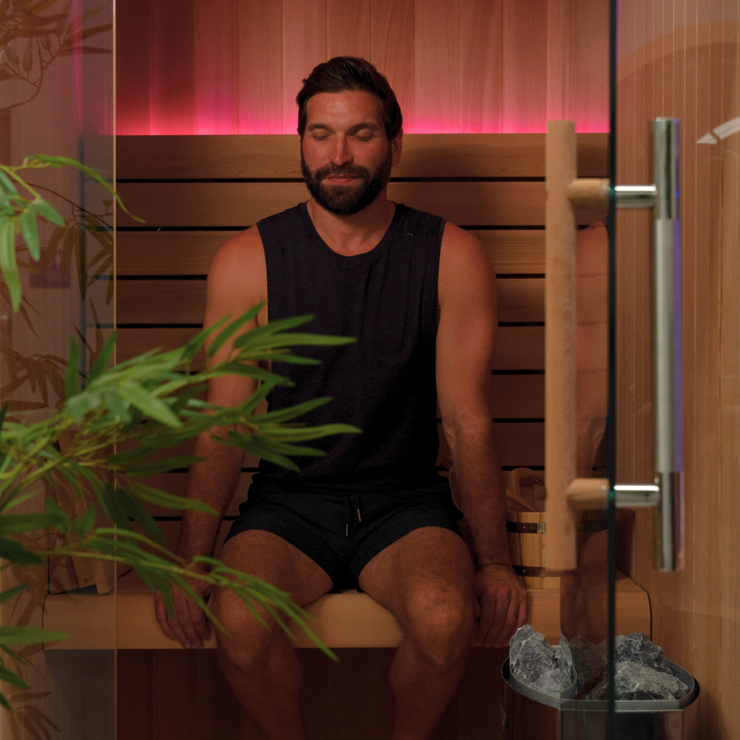 Man sitting inside a wooden sauna with plants around