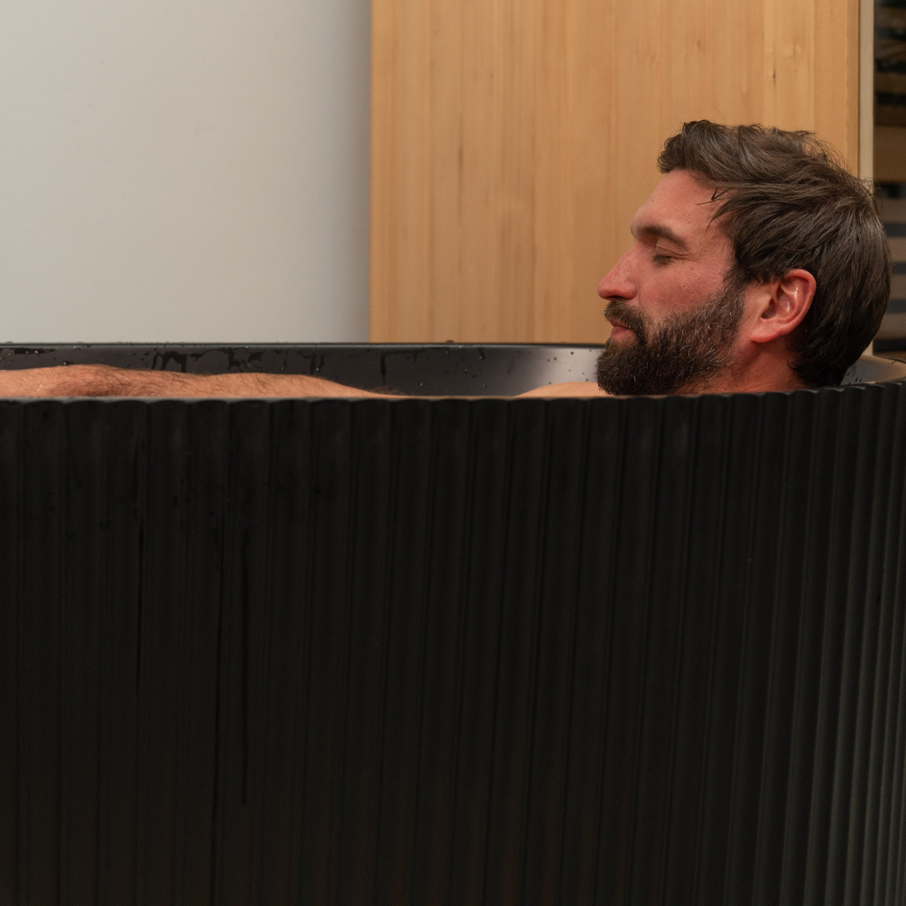 Man with a beard sitting in a black bathtub.