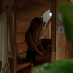 Woman sitting inside a wooden sauna with a towel hanging on the side.