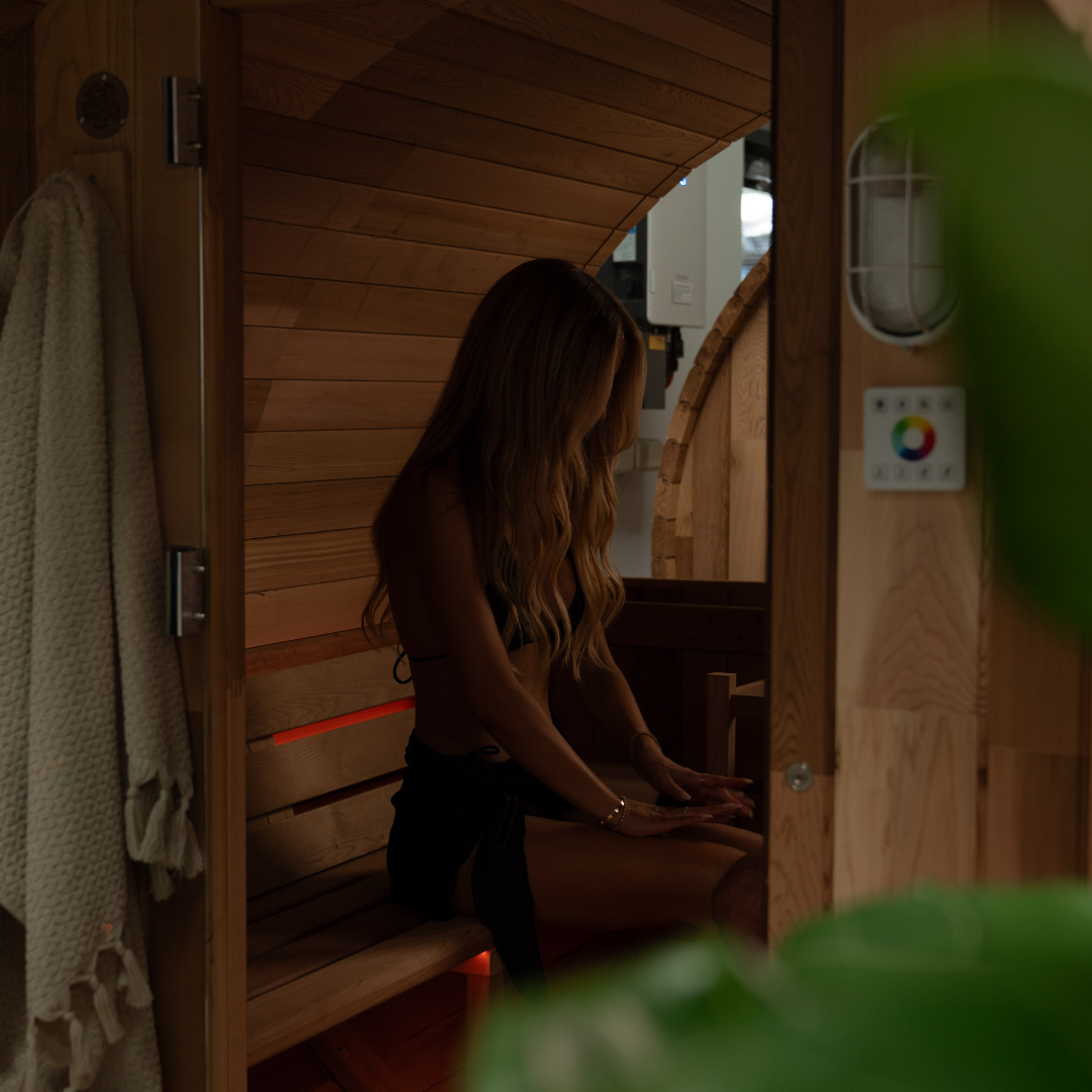 Woman sitting inside a wooden sauna with a towel hanging on the side.