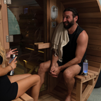 Two people in a sauna with one person holding a towel over their shoulder.