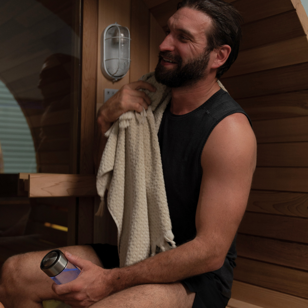Man sitting in a sauna holding a towel and a water bottle
